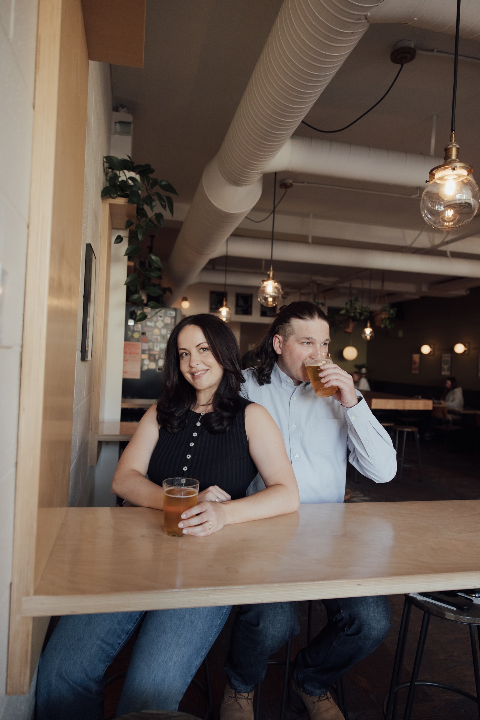 Briana and Ethan at a tall wooden table in a taproom, each holding a glass of beer.